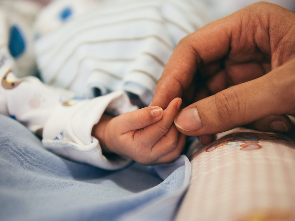Vuxen hand håller en nyfödd bebis hand