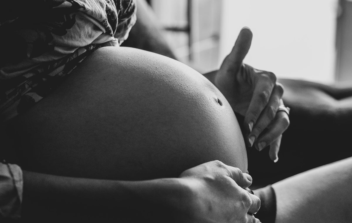 Svartvit bild av en gravid mage med händer runt