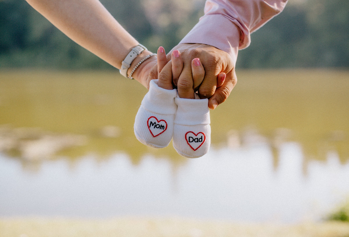 Två personer håller varsin liten babysocka framför en sjö